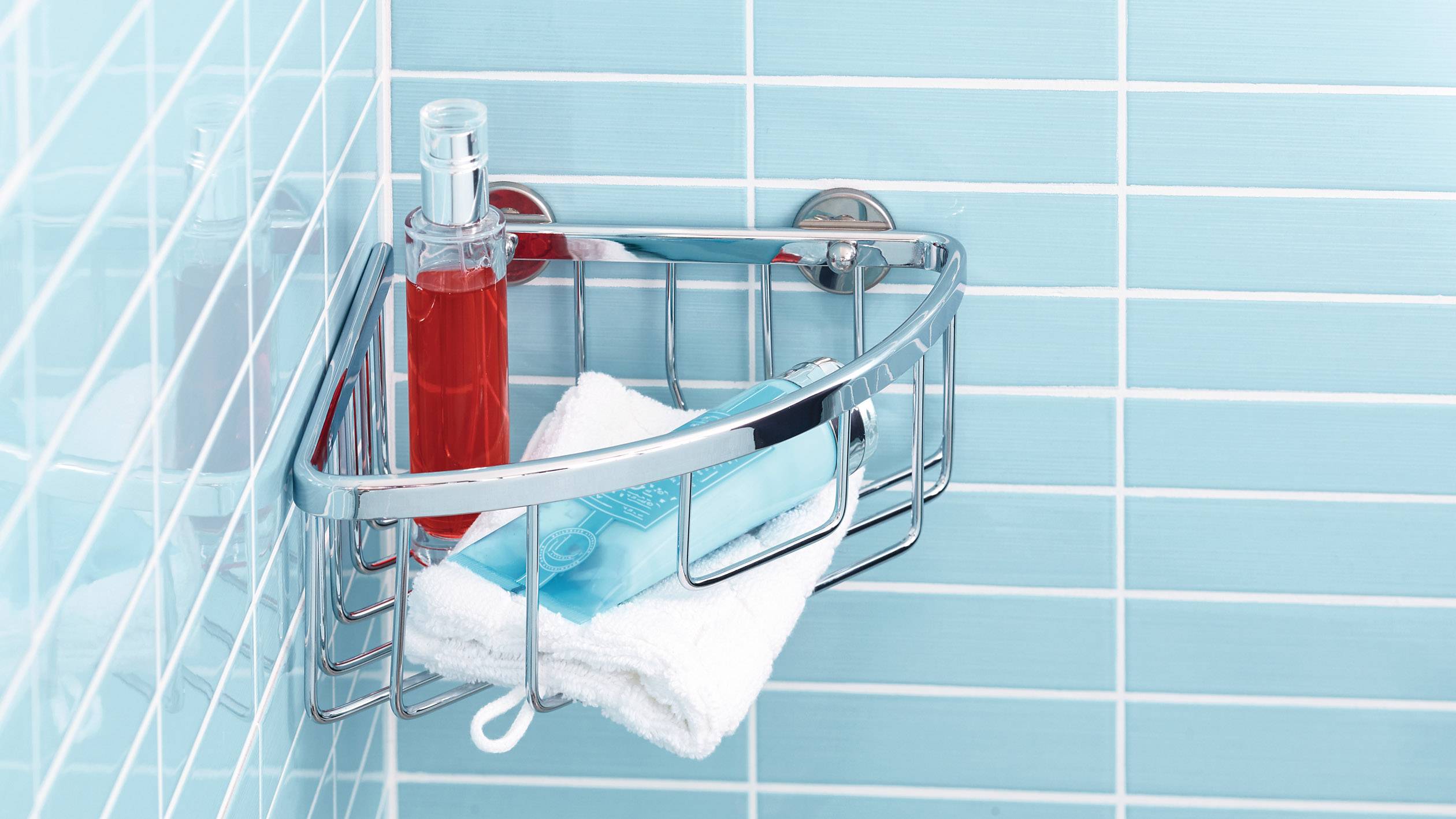 Étagère de douche avec du shampoing rouge et bleu et une serviette blanche sur un mur carrelé turquoise.