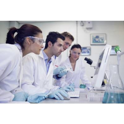 Quatre scientifiques en blouses de laboratoire et lunettes de protection travaillent sur un ordinateur dans un laboratoire, avec des tubes à essai en arrière-plan.