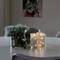 Des bougies avec une guirlande lumineuse brillent sur une table à côté d'une plante, avec un tableau en arrière-plan sur le mur.