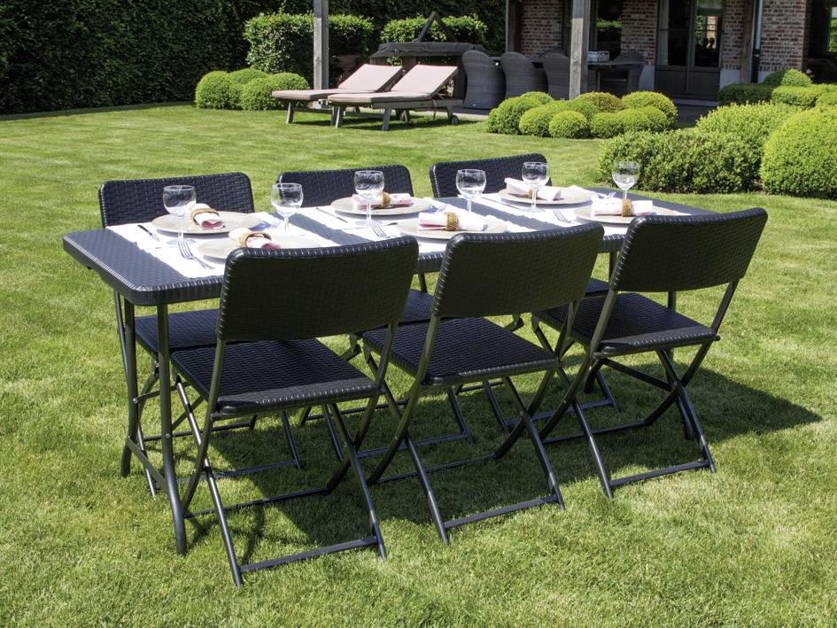 Une table de jardin avec six chaises est placée sur une pelouse. Des assiettes et des verres sont disposés sur la table, et un pavillon se trouve en arrière-plan.