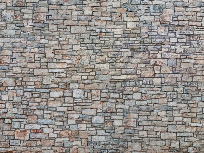 Mur de pierre avec des briques irrégulières et multicolores, principalement dans des tons de gris, pour un aspect rustique et robuste.