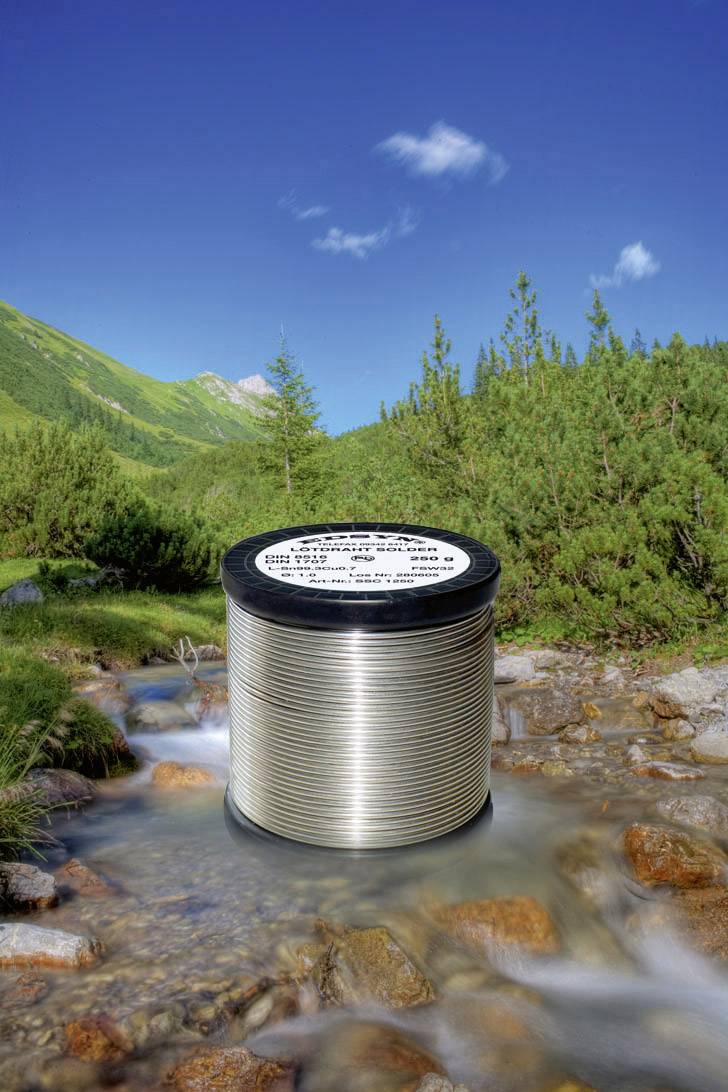 Un rouleau de fil d'argent trône au milieu d'un ruisseau de montagne peu profond, entouré de collines verdoyantes et d'un ciel bleu limpide.