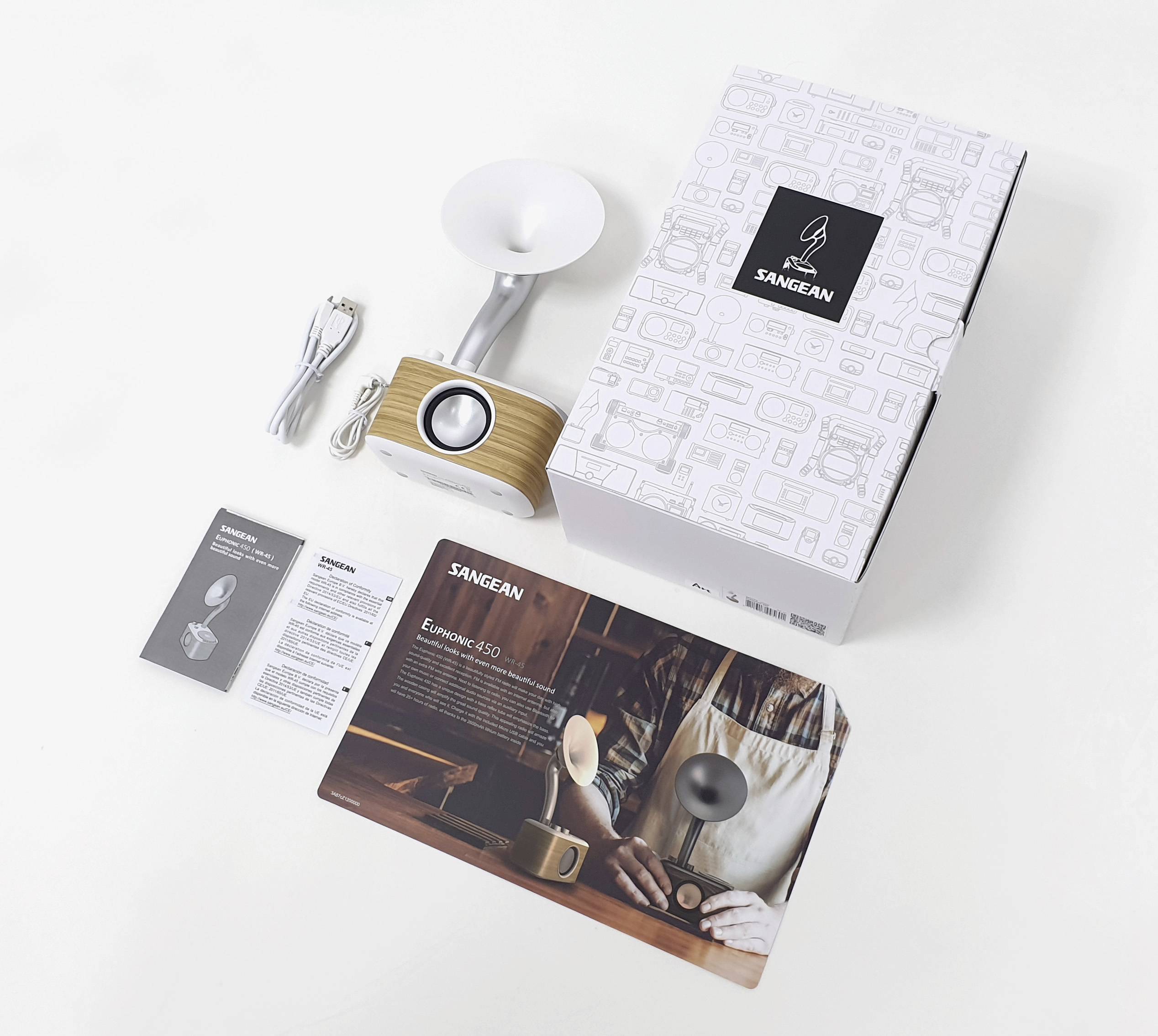 Un emballage contenant un petit haut-parleur, un câble USB et des instructions. Le design est élégant, dans des tons blanc et imitation bois.