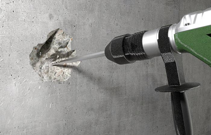 Perceuse perçant un trou dans un mur en béton. La poussière et les débris volent du mur. Outil avec boîtier vert.