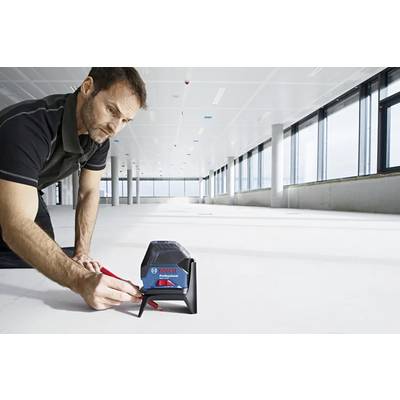 Une personne utilisant un outil de niveau laser sur un grand sol vide pour garantir l'alignement et la précision dans la construction. Une lumière naturelle vive remplit l'espace.