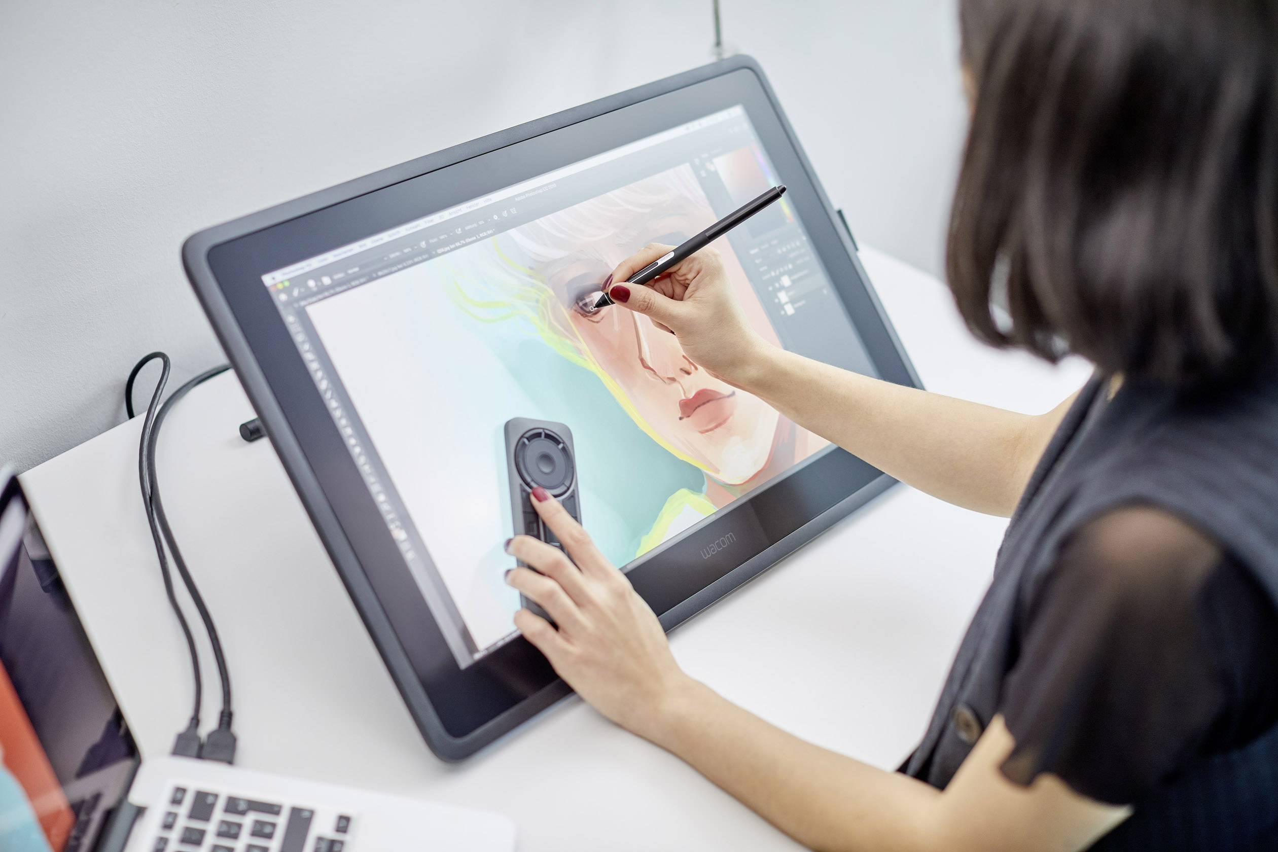 Une personne dessine un portrait numérique d'un visage sur une tablette graphique. Un ordinateur portable est posé à côté de la tablette.