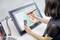Une personne dessine un portrait numérique d'un visage sur une tablette graphique. Un ordinateur portable est posé à côté de la tablette.