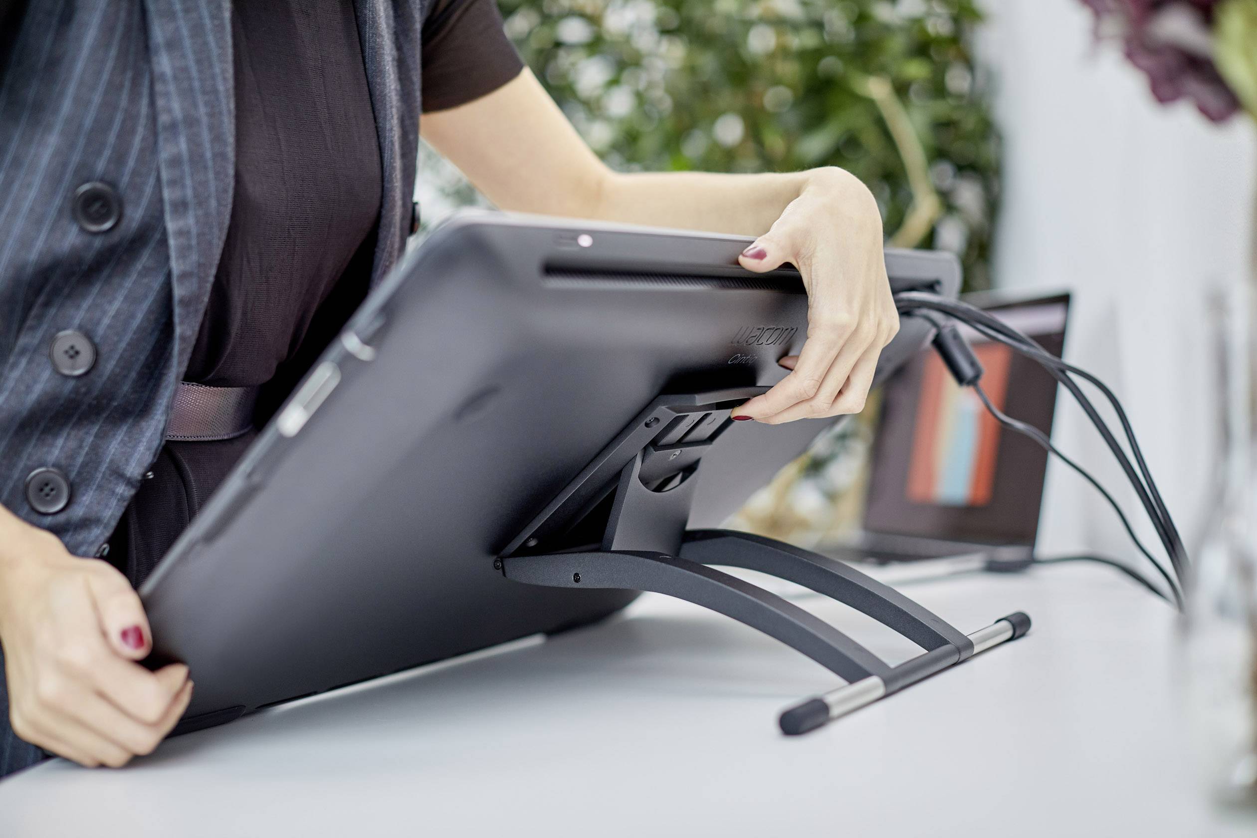 Une personne pose une tablette graphique sur un bureau. Un ordinateur portable avec un logiciel de graphisme ouvert est visible en arrière-plan.