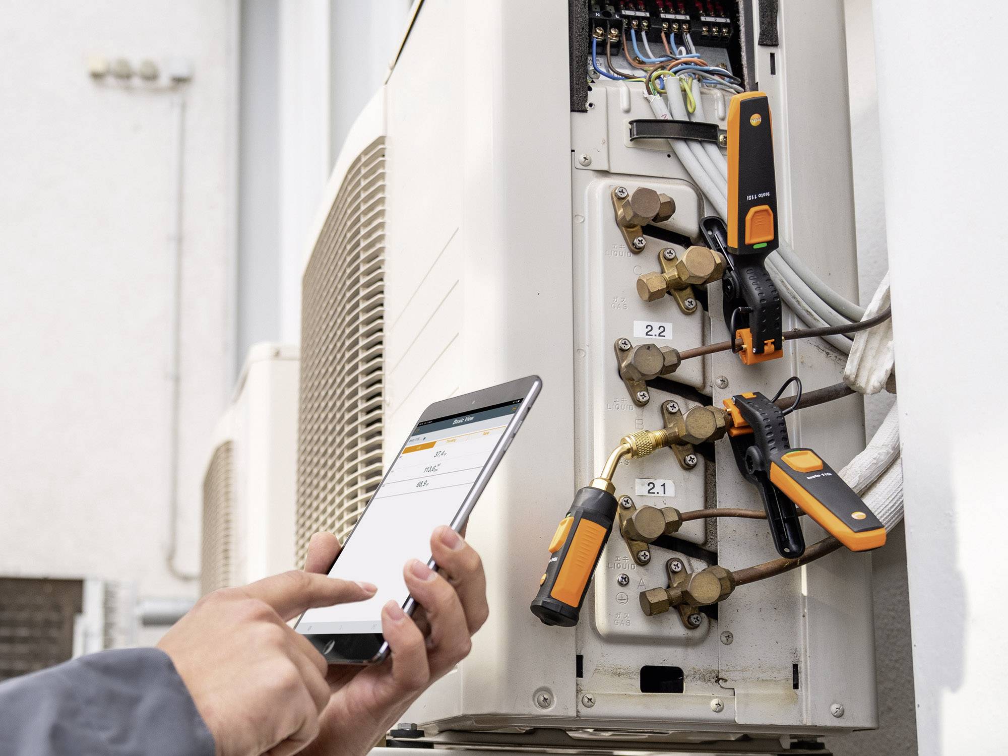 Un technicien utilise une tablette pour commander un dispositif de climatisation ouvert, montrant plusieurs tuyaux et vannes.