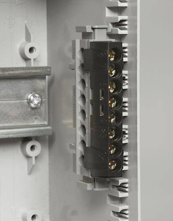 Un gros plan d'un boîtier de distribution électrique avec une barrette de bornes noire sur une plaque métallique grise.