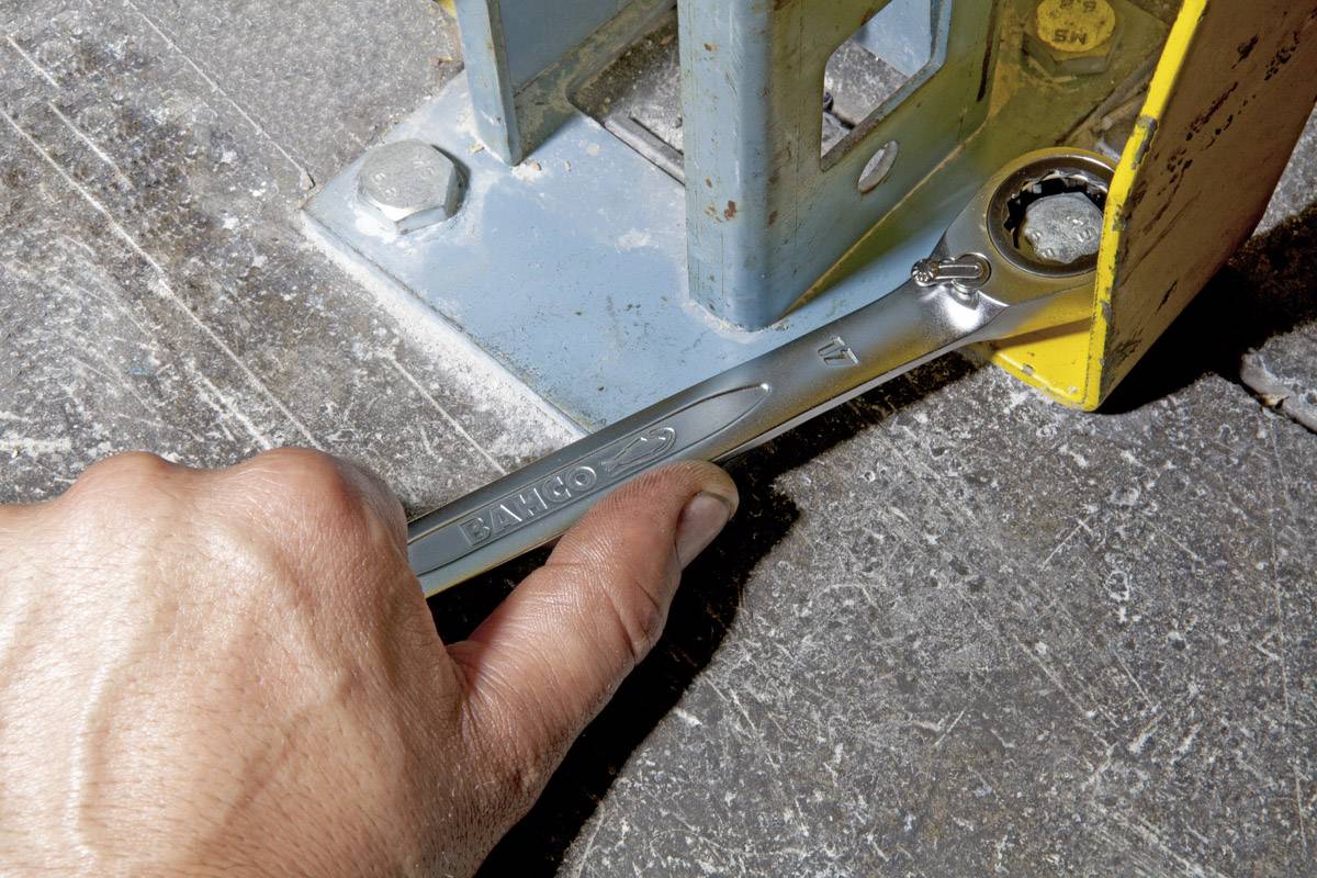 Une main utilise une clé pour serrer un boulon sur un support de machine en métal reposant sur un sol en béton.
