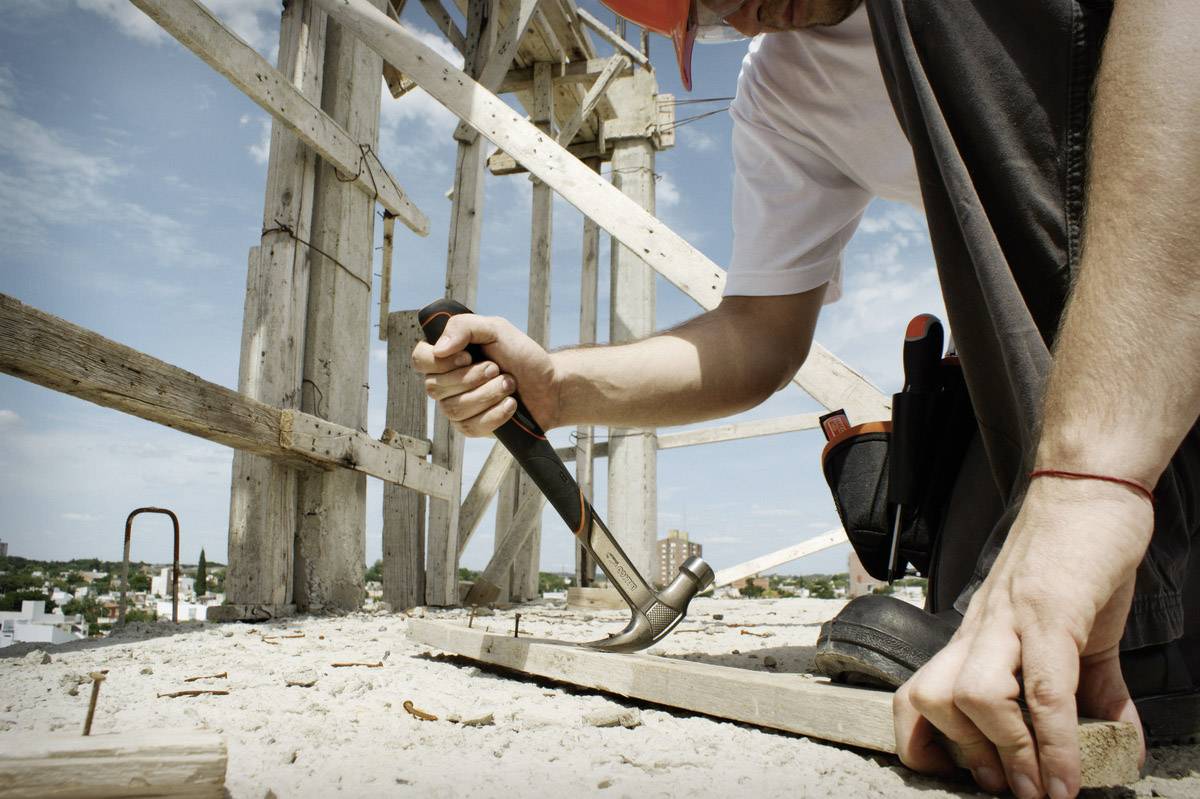 Une personne en tenue de travail enfonce un panneau sur un chantier de construction. Un échafaudage est visible en arrière-plan.
