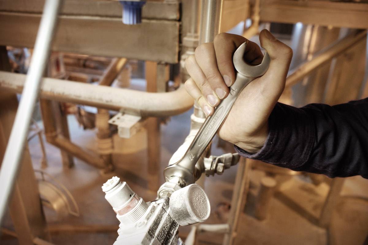 Une main tenant une clé à molette et ajustant une conduite industrielle, illustrant un travail technique dans un environnement industriel.