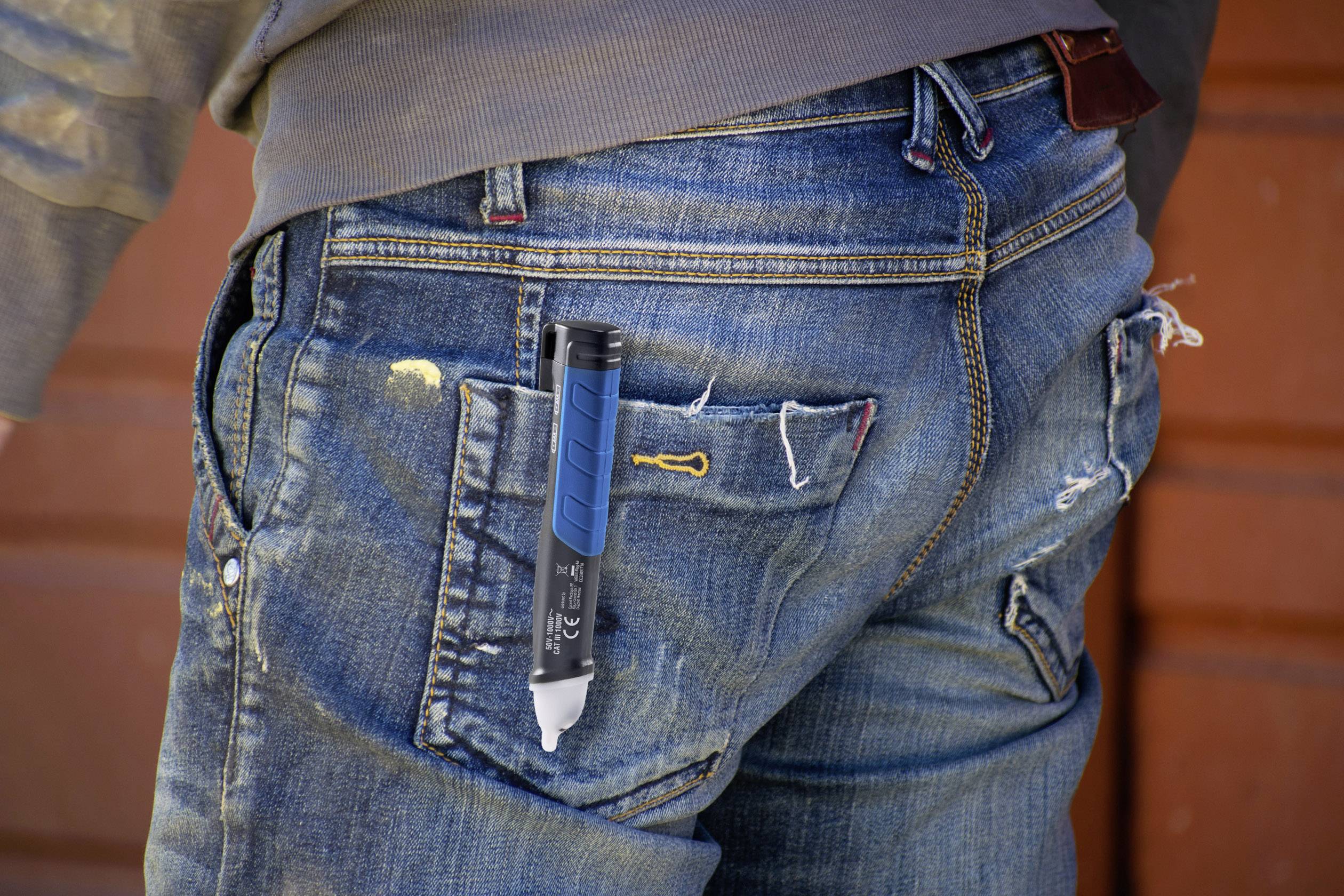 Une personne portant un jean bleu déchiré, avec un stylo bleu dépassant de la poche arrière. L'arrière-plan est flou.