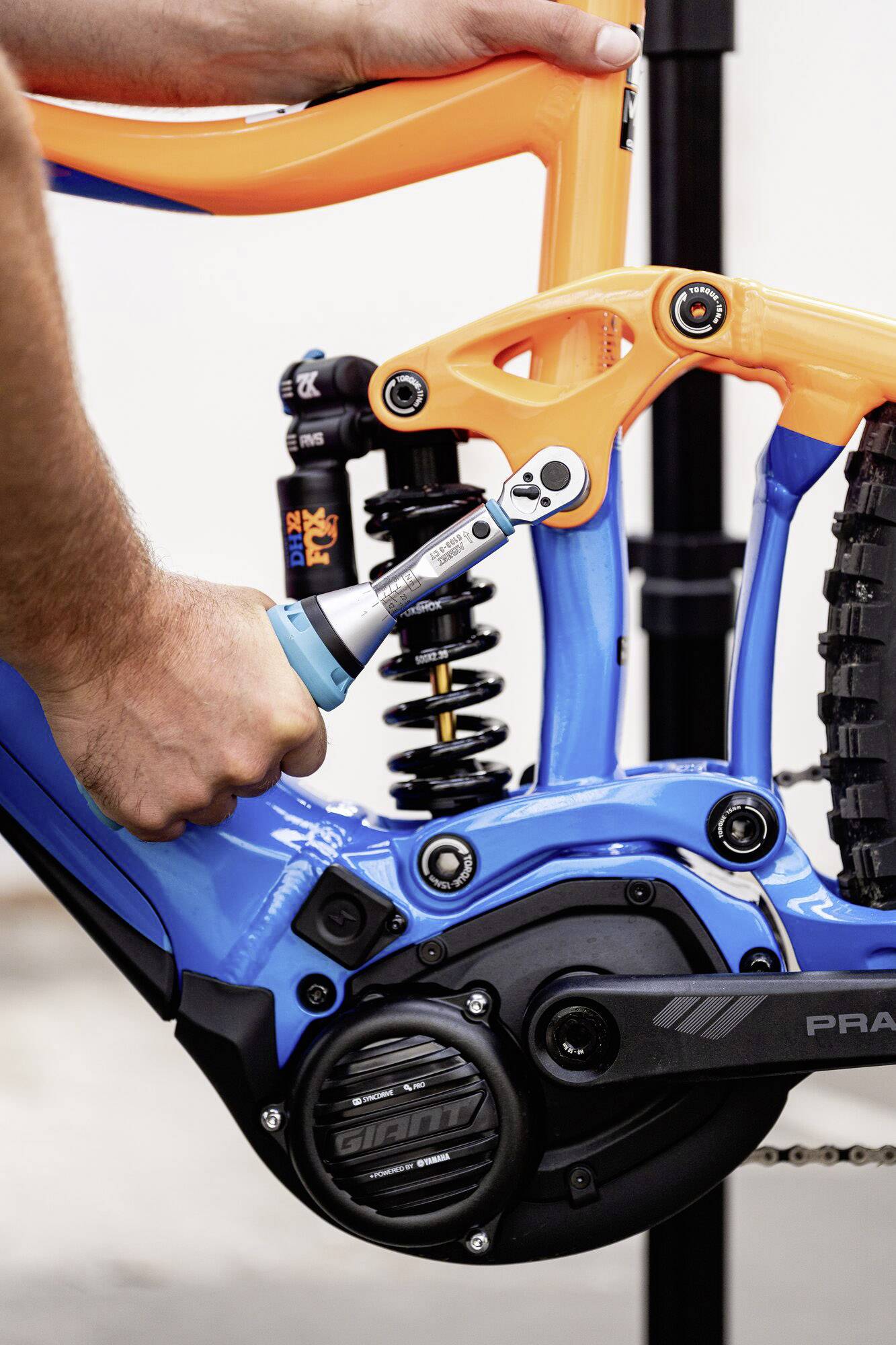 Un mécanicien serre la vis avec une clé dynamométrique sur un cadre de vélo orange et bleu. Le vélo est monté sur un support.