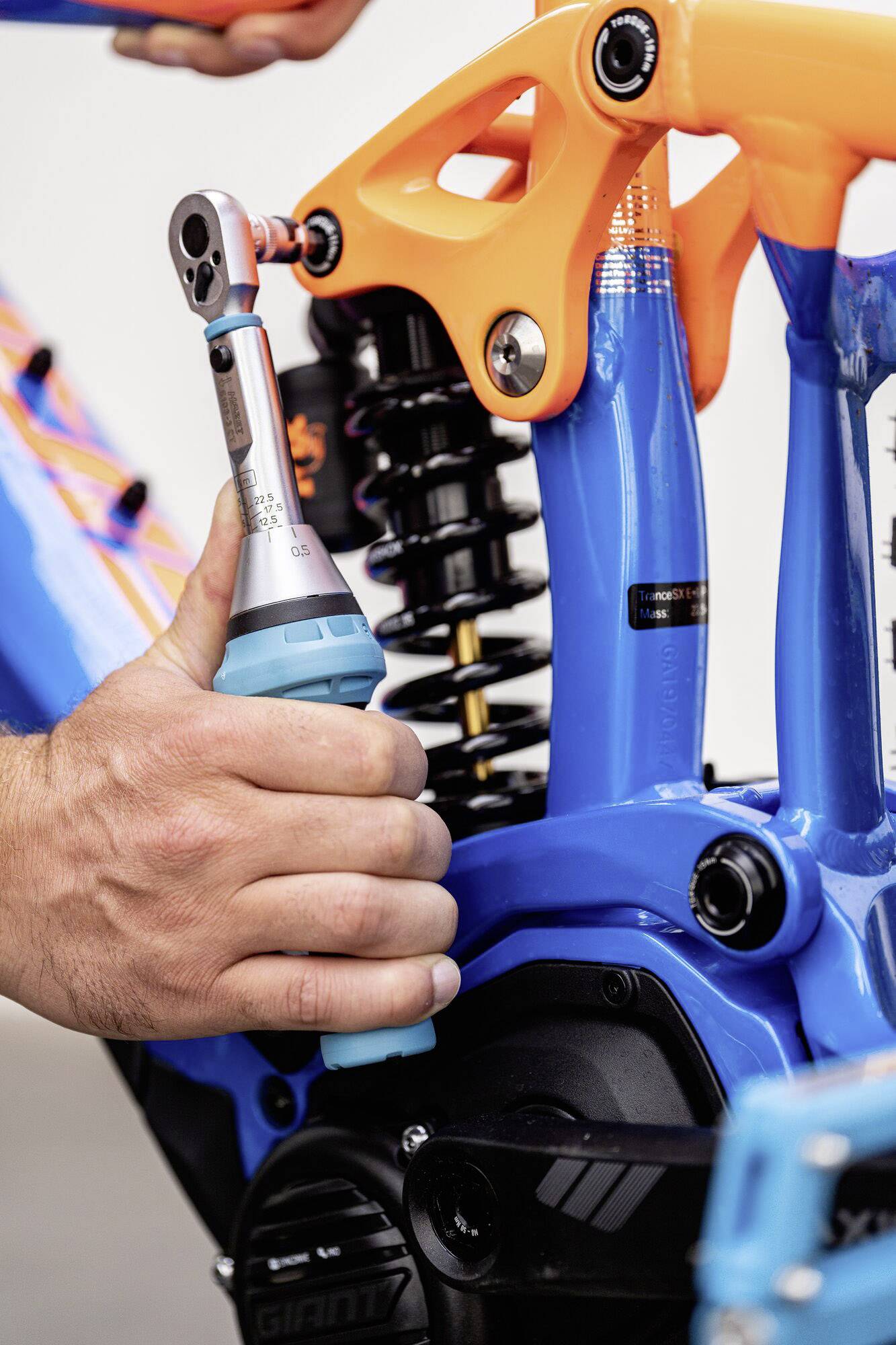 Gros plan sur une personne serrant une vis avec un tournevis sur un cadre de vélo. Le cadre est bleu et orange.