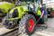 Un mécanicien répare un grand véhicule agricole dans un atelier. Le tracteur est vert avec une roue rouge.