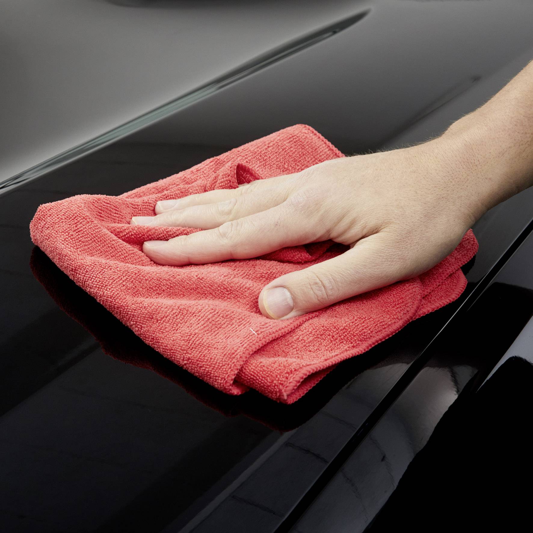 Une main nettoie la surface brillante d'une voiture avec un chiffon rouge.