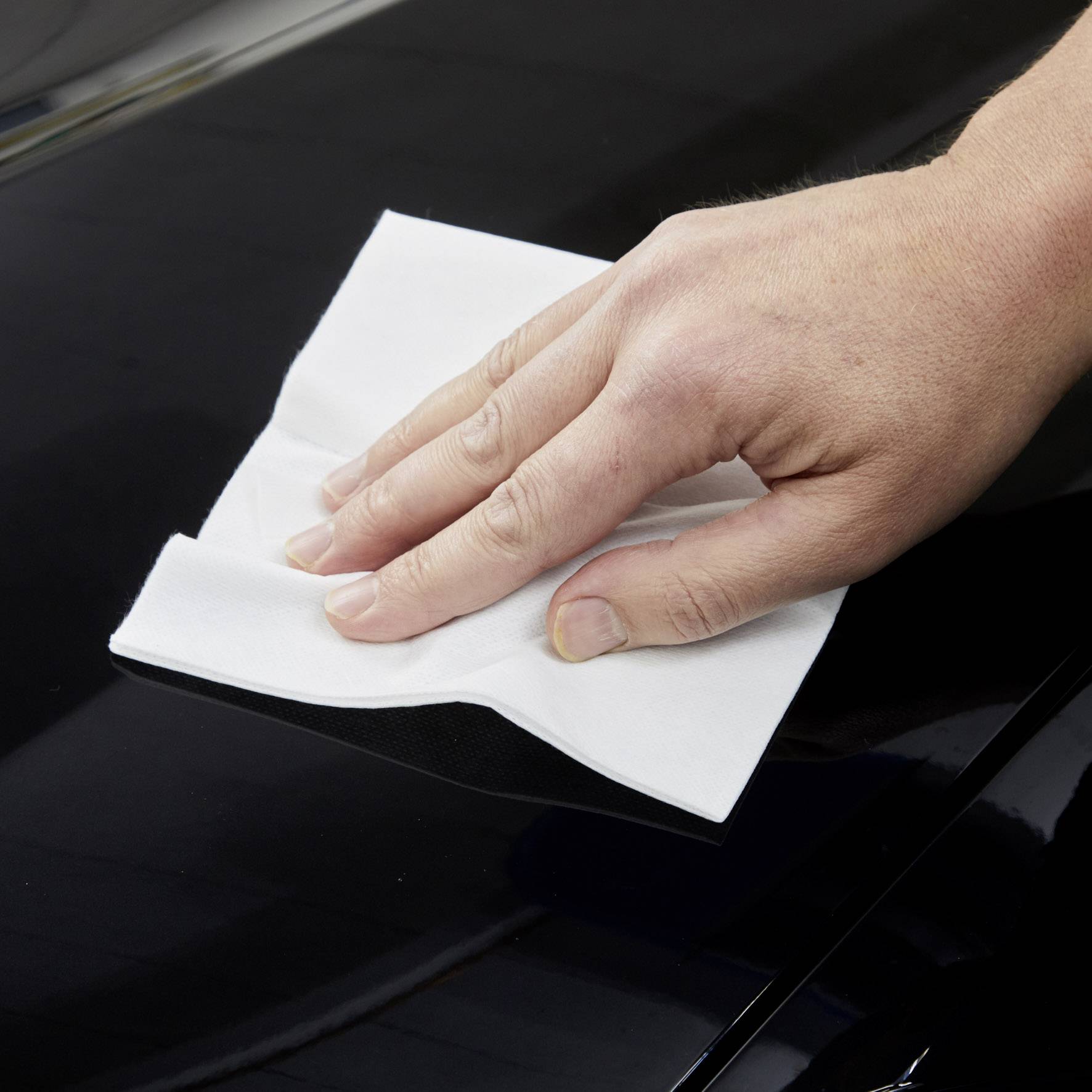 Une main essuie une surface brillante et noire avec un chiffon blanc, la faisant briller.