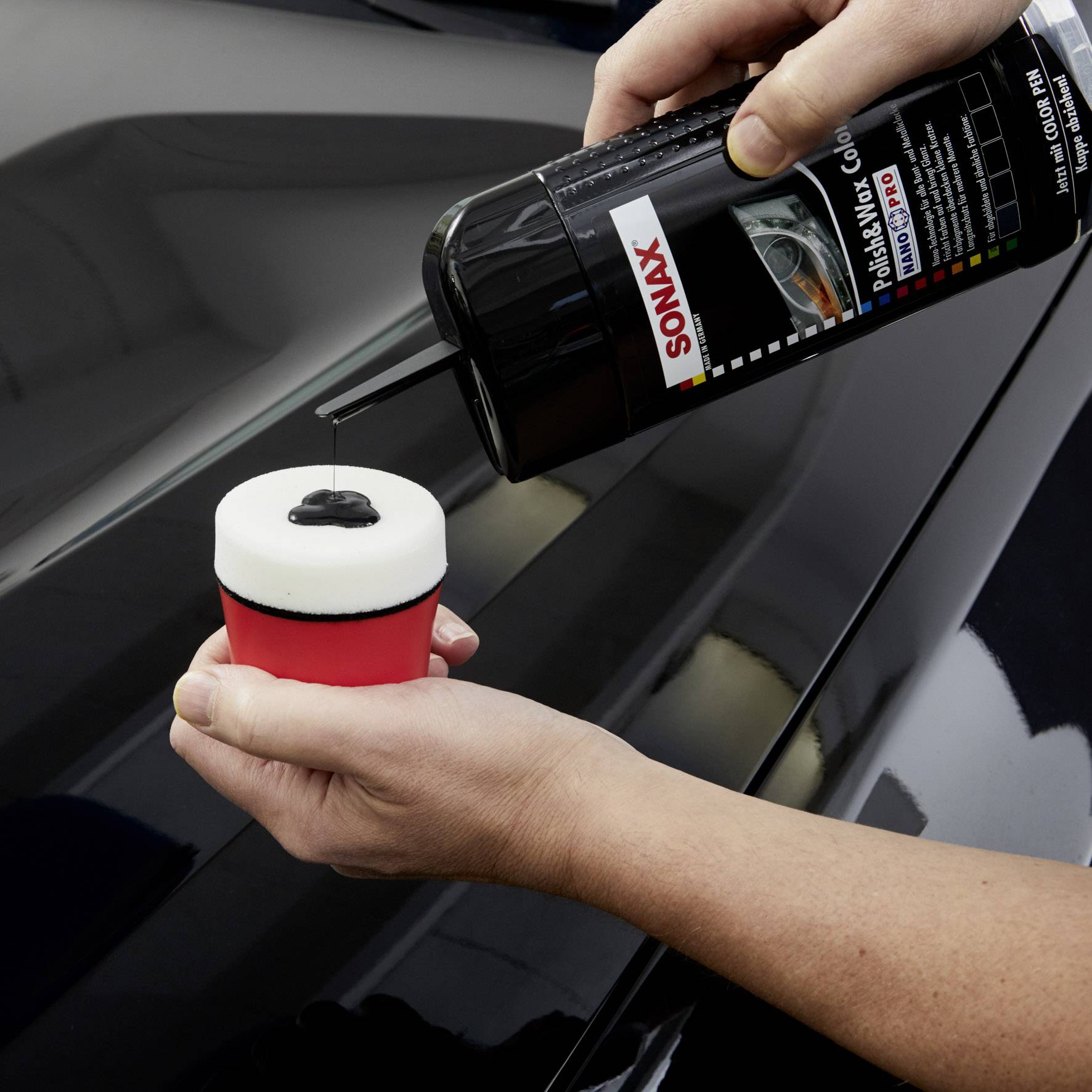 Une personne tient un tampon de polissage doux et applique du polish pour voiture avec une bouteille, afin de prendre soin de la surface de peinture d'un véhicule.