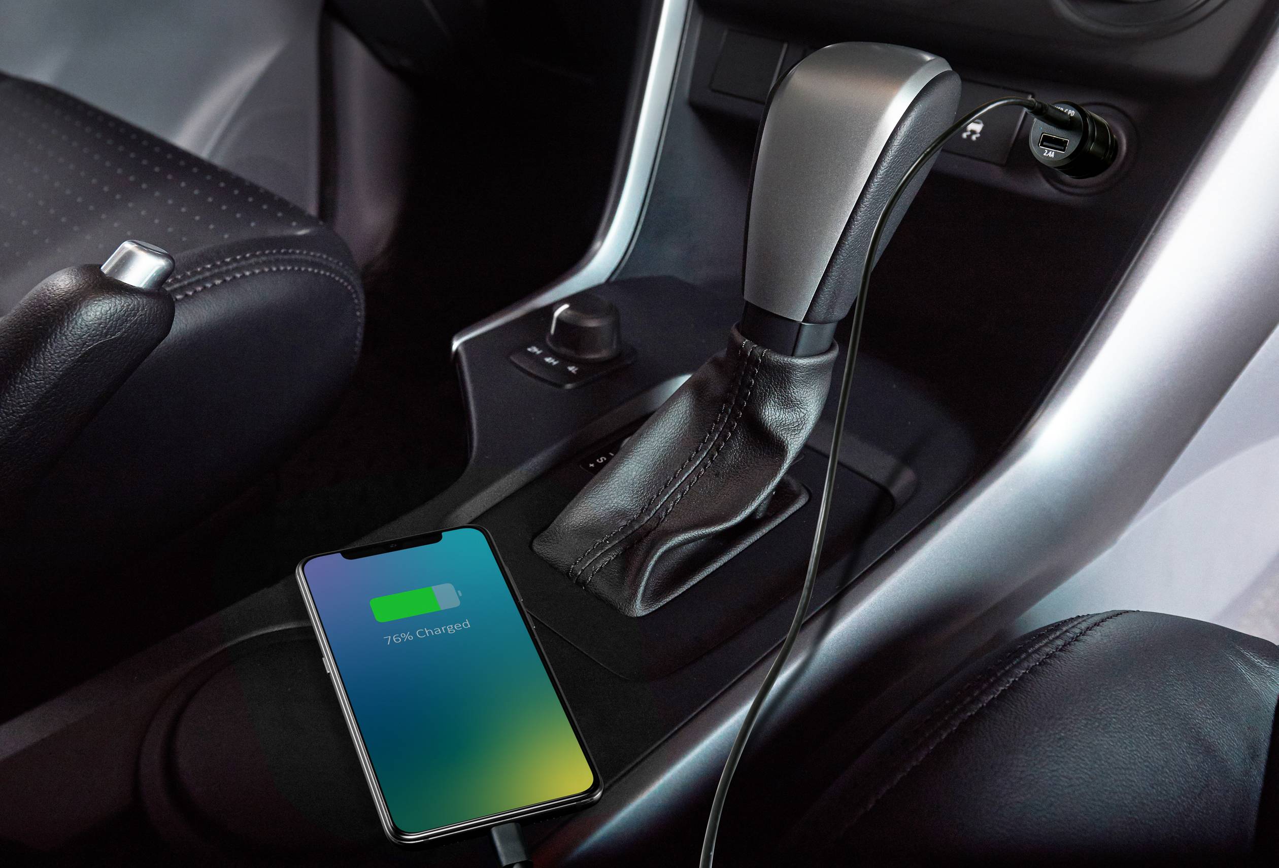 Un smartphone est en train de se charger dans une voiture. Il est posé à côté du levier de vitesses sur la console centrale. L'écran indique que l'appareil est en cours de chargement.