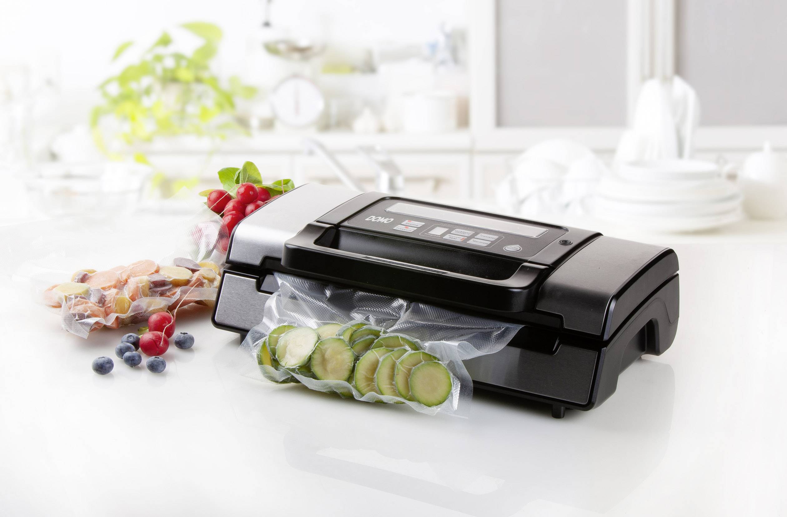 Appareil de mise sous vide sur une table de cuisine, scellant des tranches fines de concombre dans un sachet. Des baies et des légumes sont disposés en arrière-plan.