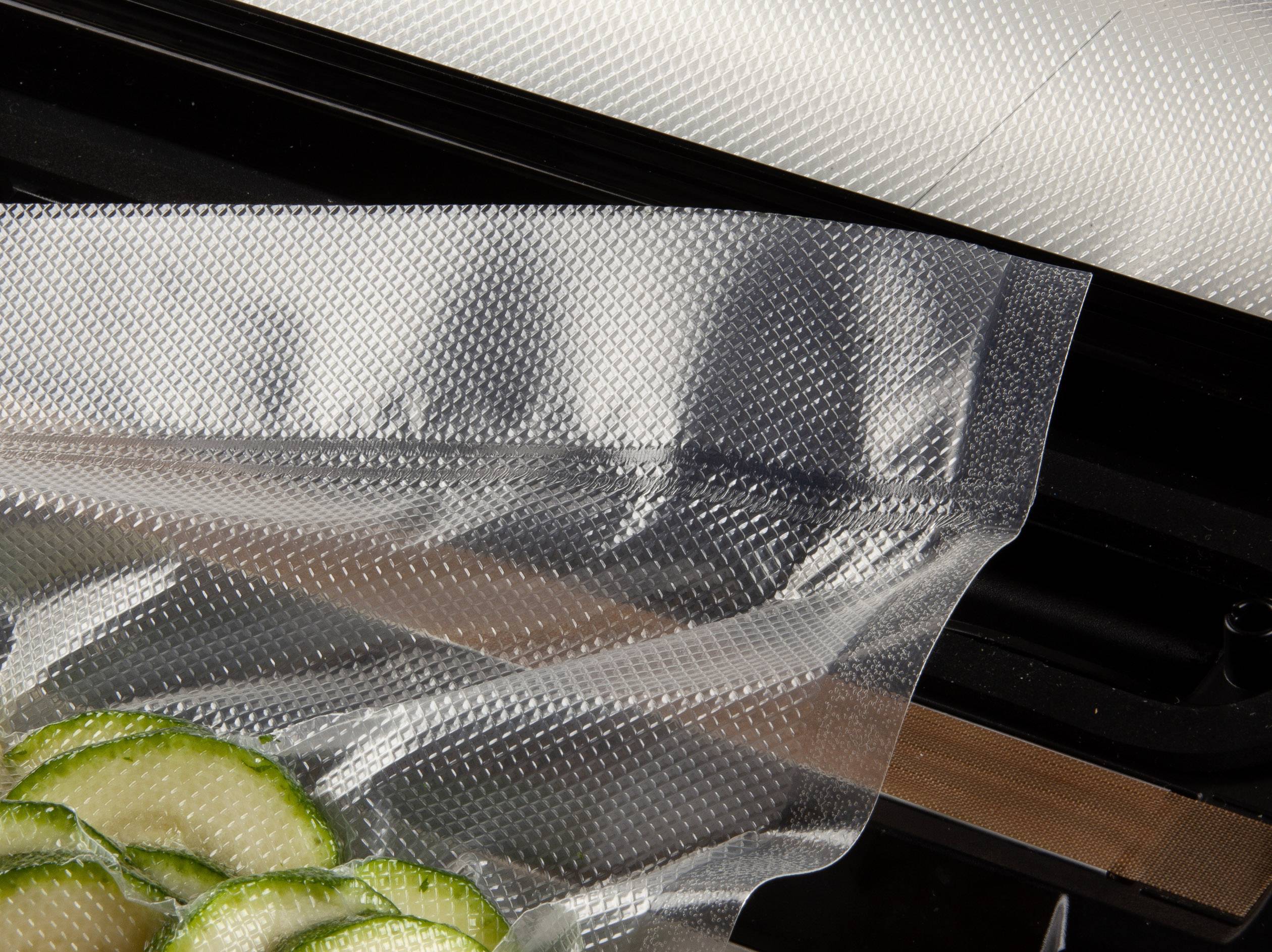 Gros plan d'un appareil de mise sous vide avec un film transparent recouvrant des tranches de concombre coupées, prêt à être scellé.