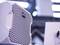 Enceinte acoustique avec design de grille alvéolaire blanche, vue de côté, dans un intérieur moderne et flou.