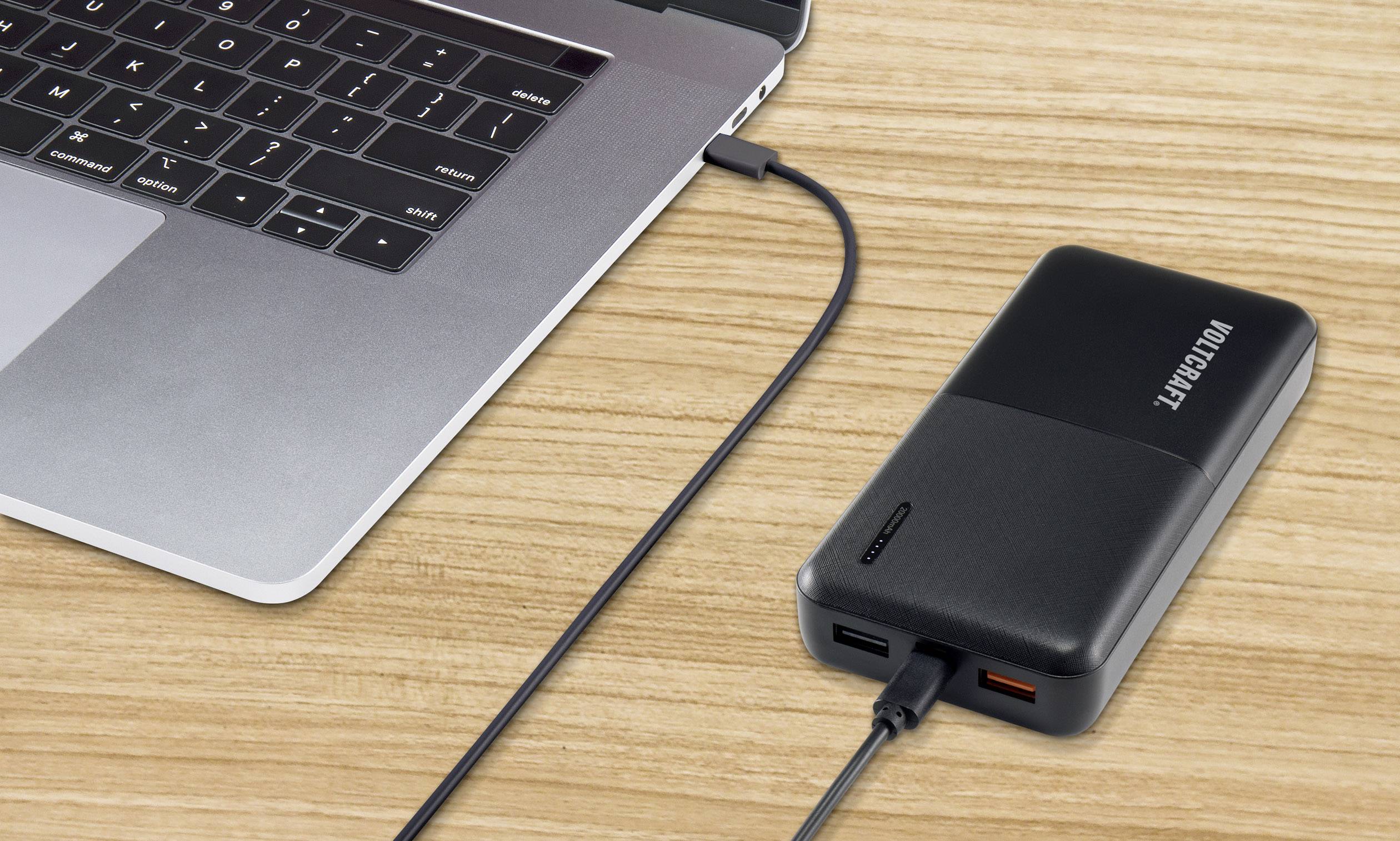 Un ordinateur portable est en train de se charger via un câble USB sur une batterie externe posée sur une table en bois.
