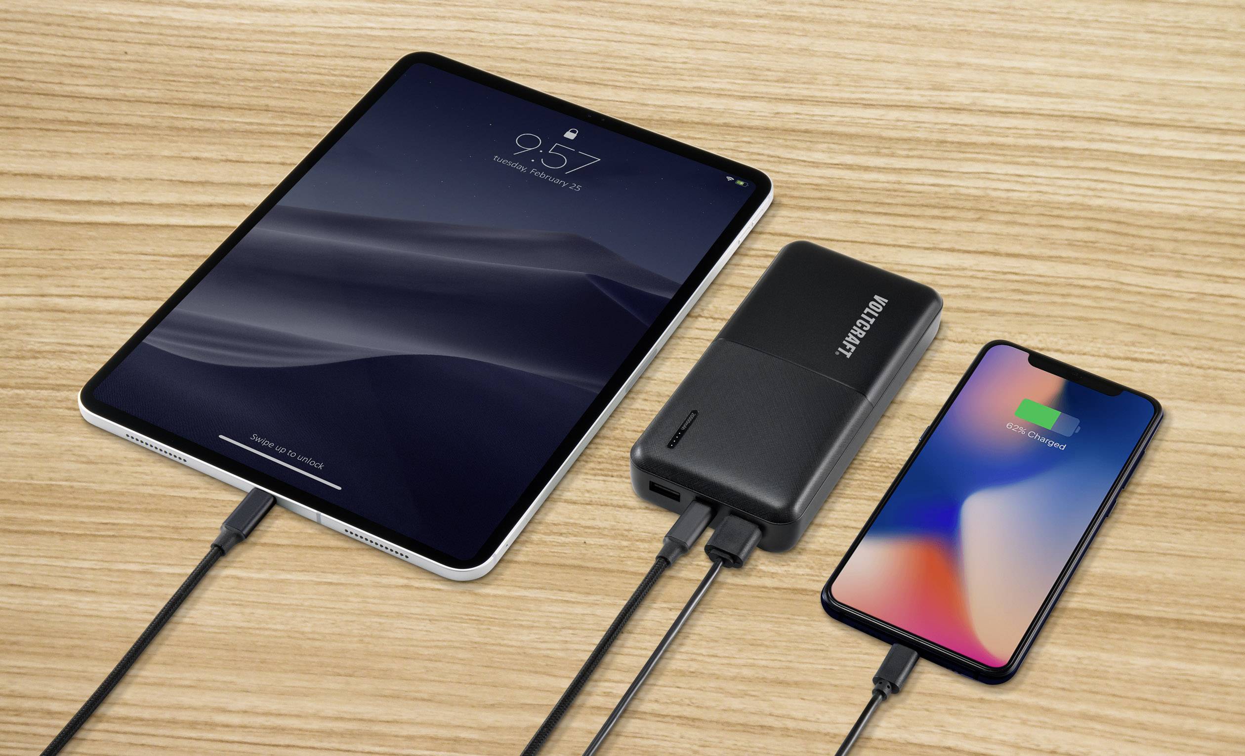 Une tablette et un smartphone sont rechargés simultanément avec une batterie externe sur une table en bois.