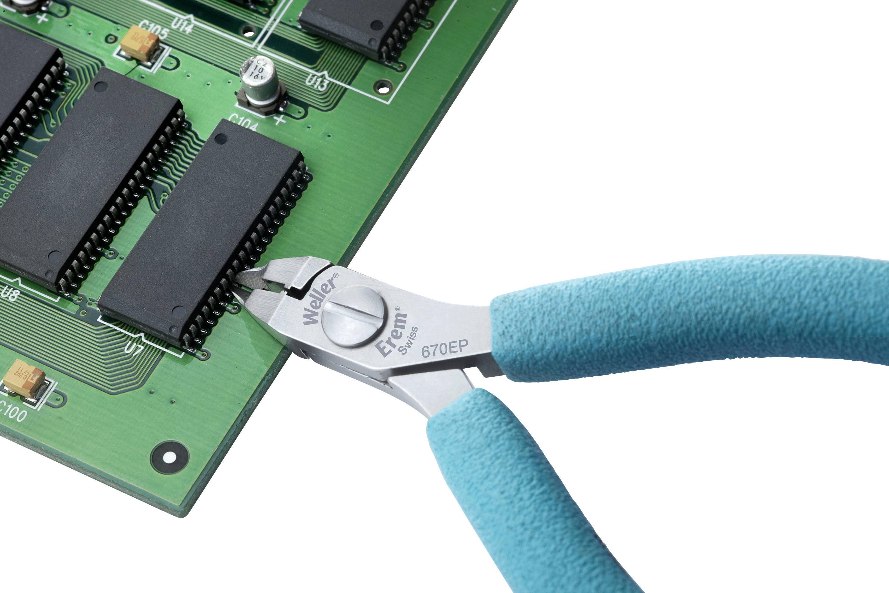 Une pince coupe des fils sur un circuit imprimé vert comportant plusieurs composants électroniques.