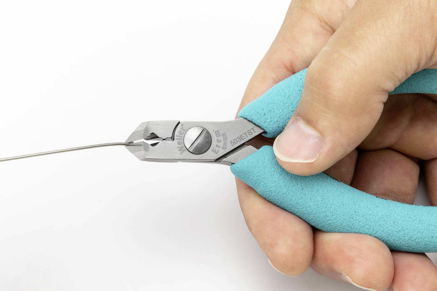Une main tient une pince avec une poignée turquoise et coupe un fil fin.