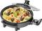 Poêle électrique avec paella : Risotto aux morceaux de poivrons verts et rouges, aux moules, aux morceaux de poulet et garni d'herbes dans un couvercle ouvert.