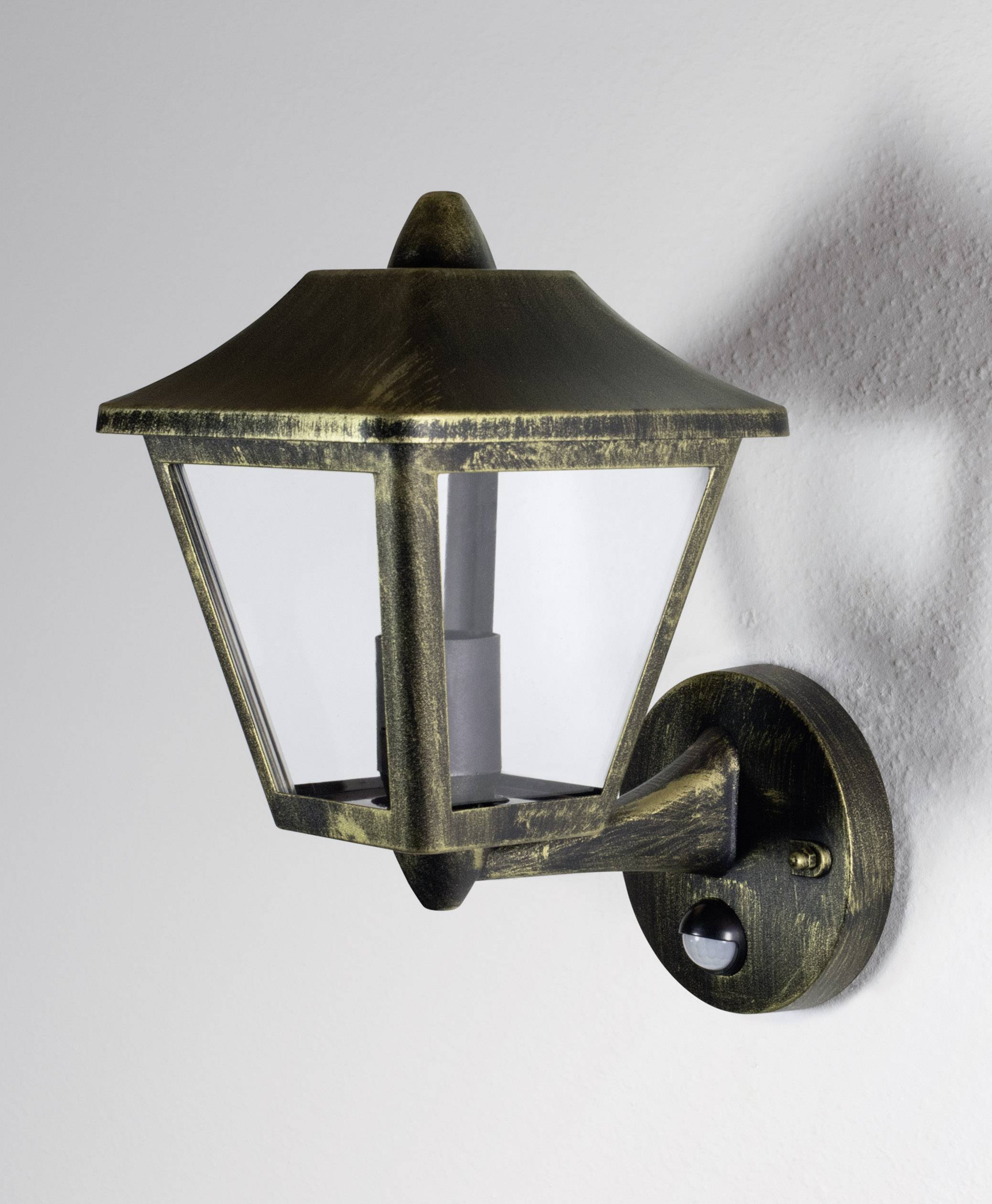 Applique murale de style antique, fixée sur un mur. L'luminaire présente une forme carrée avec des panneaux vitrés et une finition en laiton ancien.