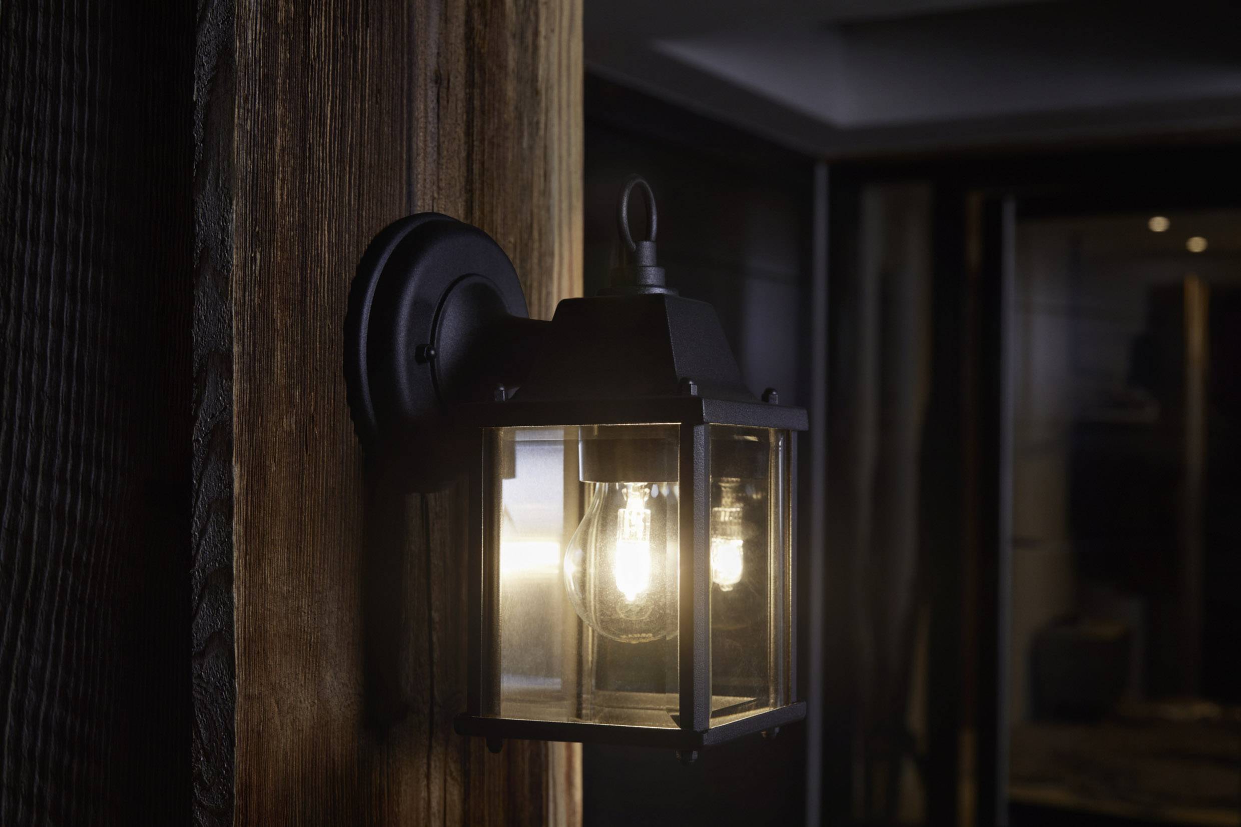 Une lanterne noire de style classique éclaire un mur en bois dans une pièce sombre.