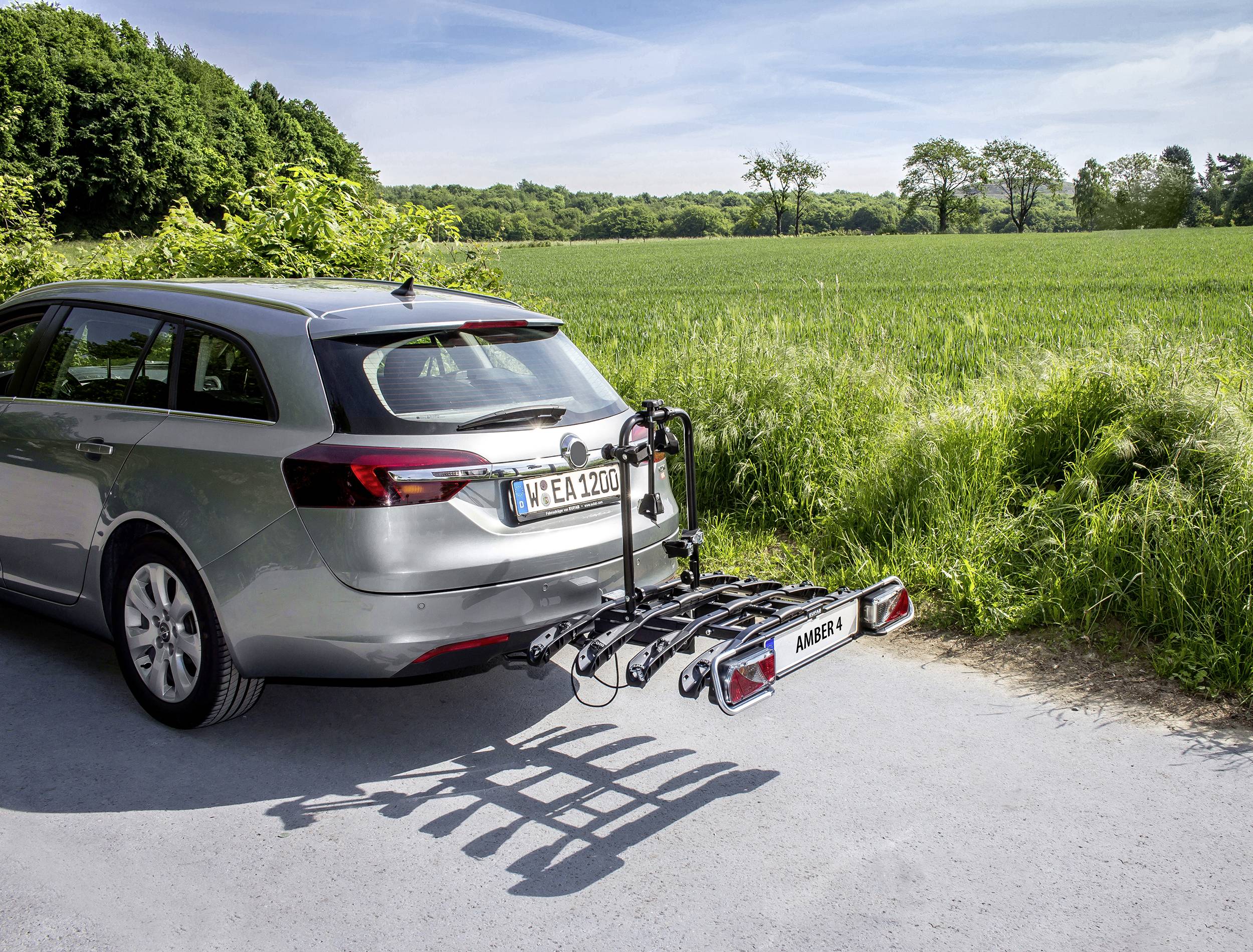 Voiture avec un porte-vélos garée sur une route de campagne en bordure de champ. Le temps est ensoleillé.