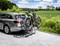 Une voiture argentée avec un porte-vélos transportant deux vélos est garée sur un chemin rural, à côté de champs verts et d'arbres.