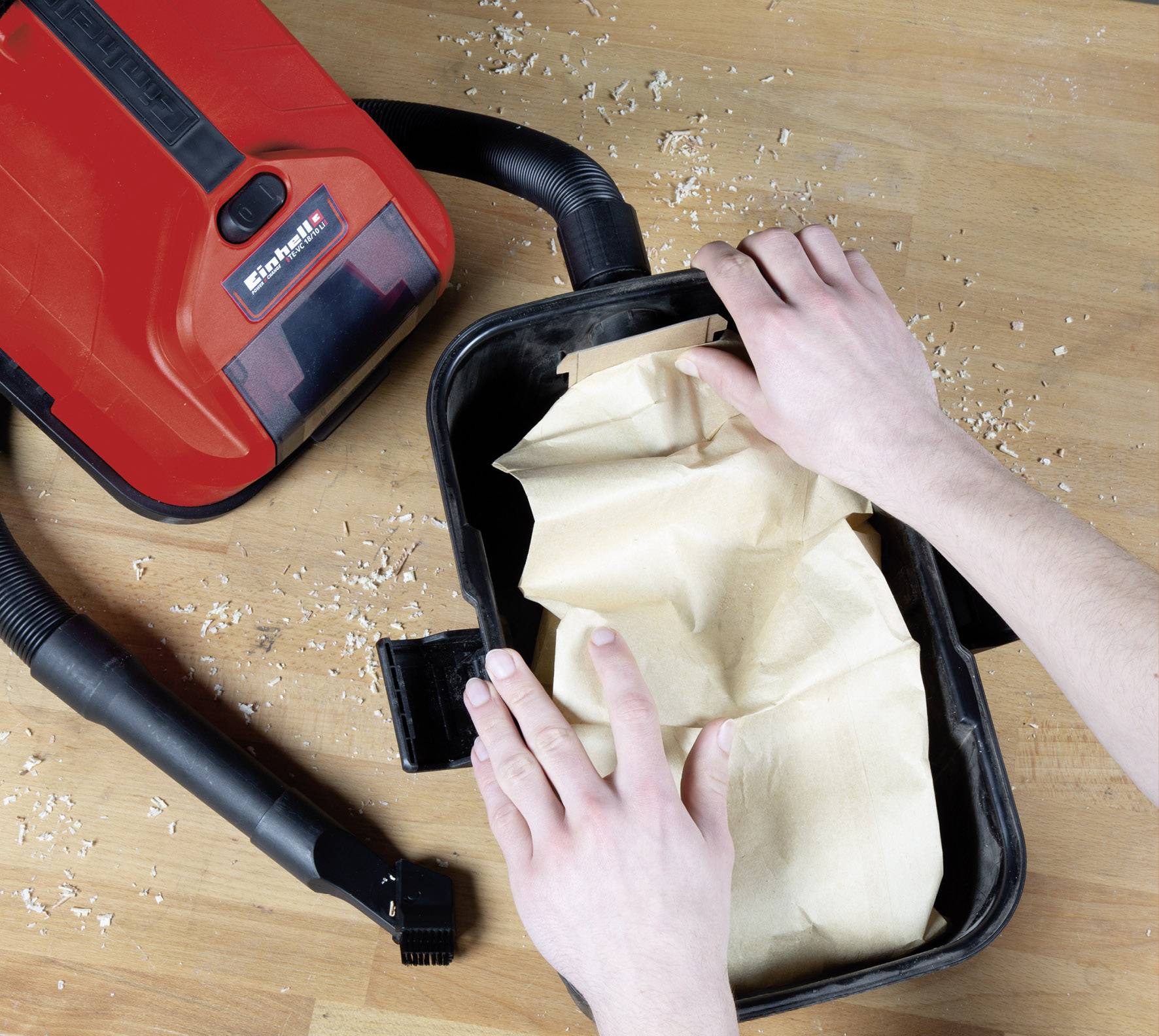 Un aspirateur industriel rouge sur un fond en bois ; des mains changent un sac à poussière.