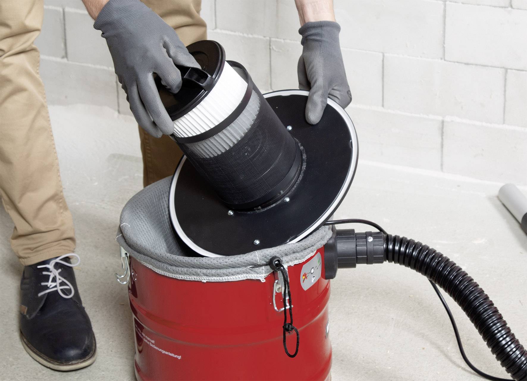 Une personne change le filtre d'un aspirateur rouge dans un environnement d'atelier.