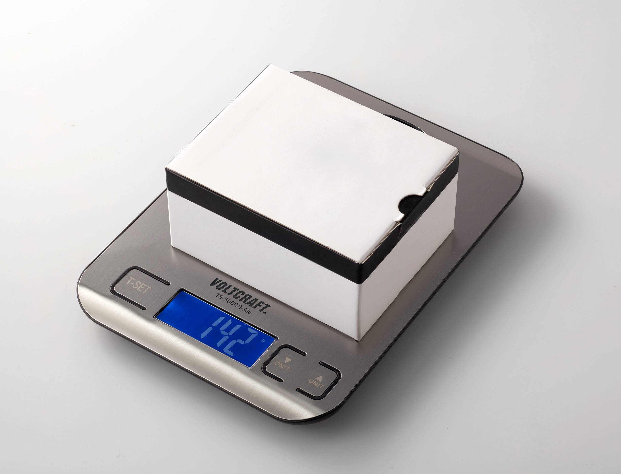 Une balance de cuisine numérique affiche un poids de 1,42 kg. Un paquet carré blanc est posé sur la balance.