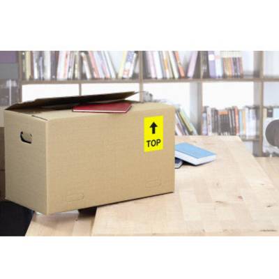 Un carton de déménagement ouvert avec une étiquette "TOP" est posé sur une table. Des étagères à livres sont visibles en arrière-plan.