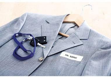 Costume gris avec badge nominatif 'M. Miller', trousseau de clés et lanière de clés bleue sur un cintre en bois.