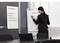 Une femme écrit sur un tableau à feuilles mobiles dans un bureau. Un tableau accroché au mur présente des étapes de projet telles que 'Potentiel de marché' et 'Groupe cible'.