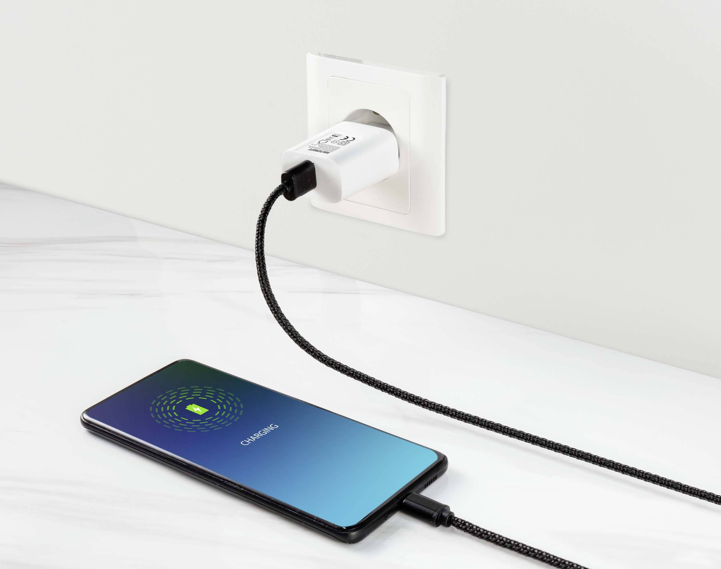 Un smartphone est en train de se charger dans une prise électrique à l'aide d'un chargeur. L'écran du smartphone affiche l'état de la charge.