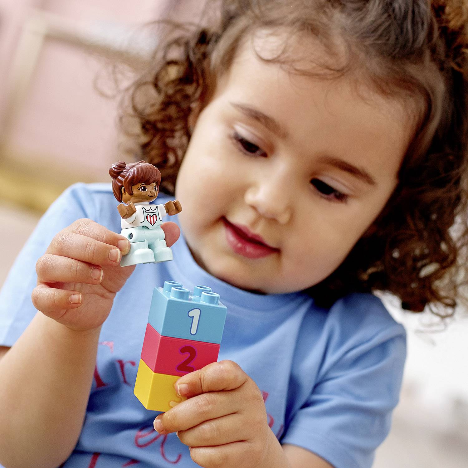 Un petit enfant tient une figurine empilable dans sa main, posée sur des blocs de construction colorés portant des chiffres.