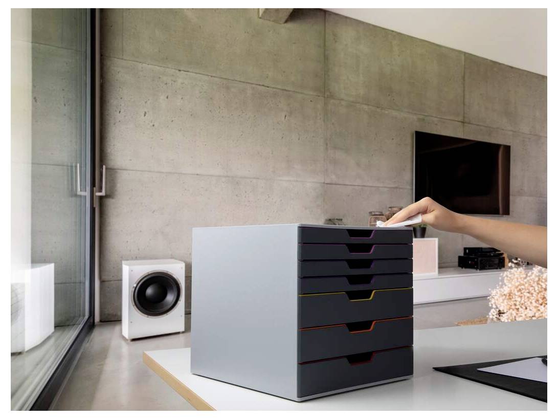 Une main se tend vers un document posé sur une unité de tiroirs moderne et multicolore dans un bureau minimaliste aux murs en béton.