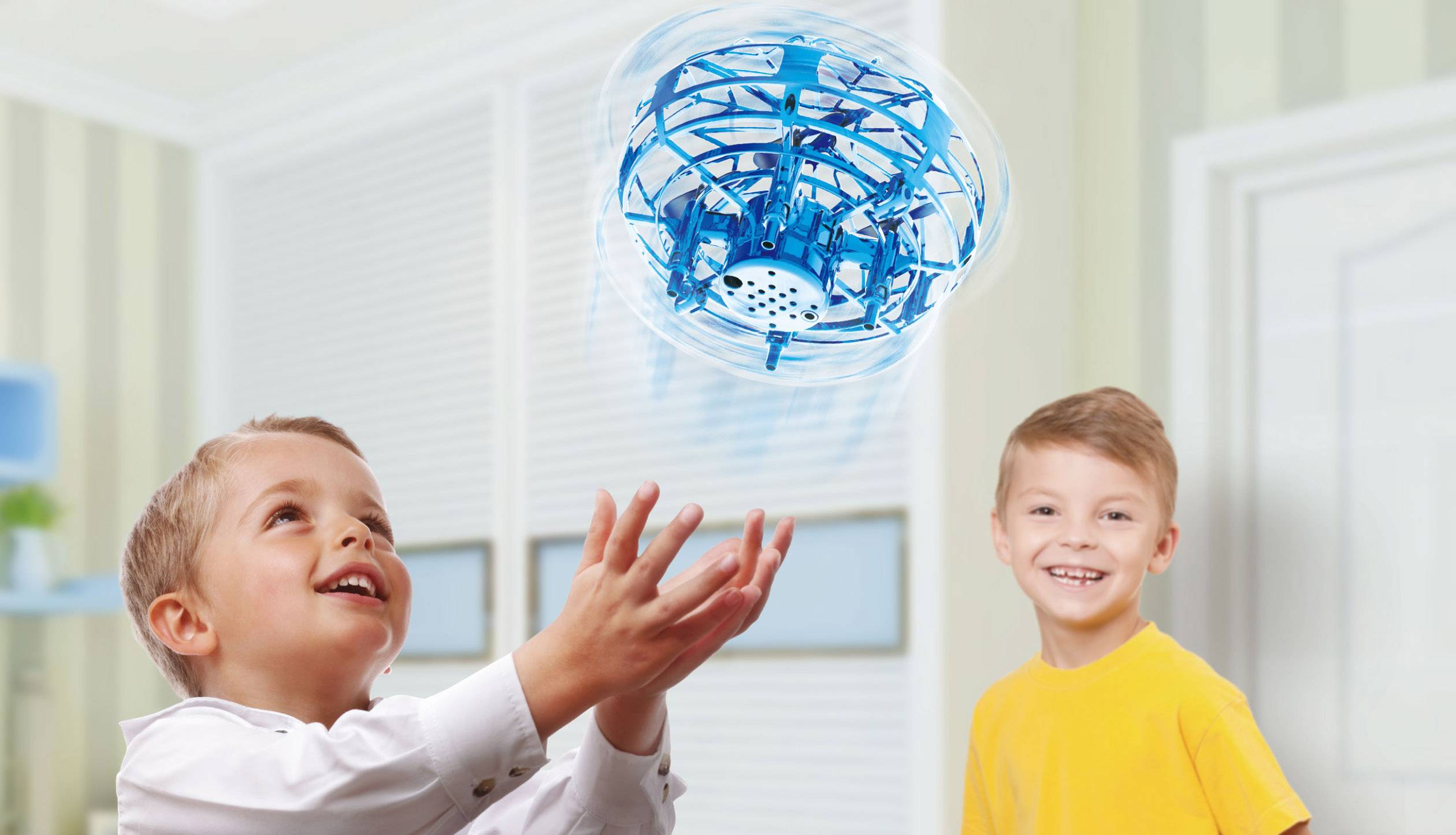 Deux enfants jouent avec un drone bleu en vol dans une pièce lumineuse. Le garçon de gauche attrape le drone, tandis que le garçon de droite sourit.