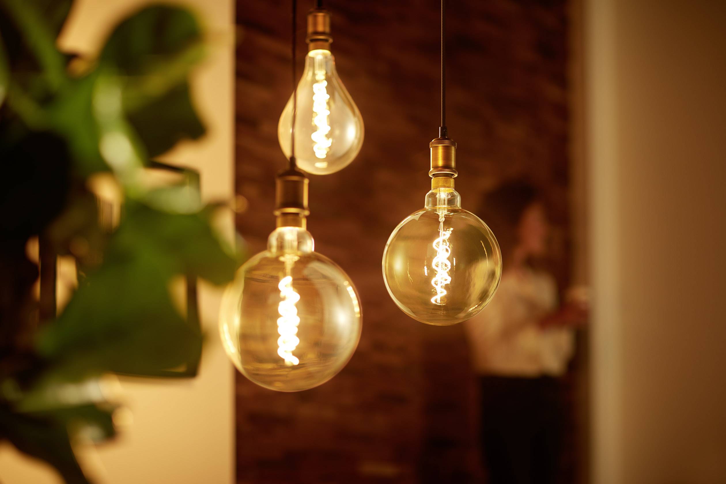 'Trois ampoules suspendues brillent d'une lumière chaleureuse dans une pièce, avec une personne floue visible en arrière-plan.'