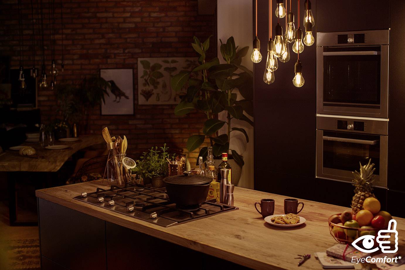 Une cuisine chaleureusement éclairée avec une cuisinière sur un îlot central, entourée d'ustensiles de cuisine variés, de fruits et d'une plante en arrière-plan.