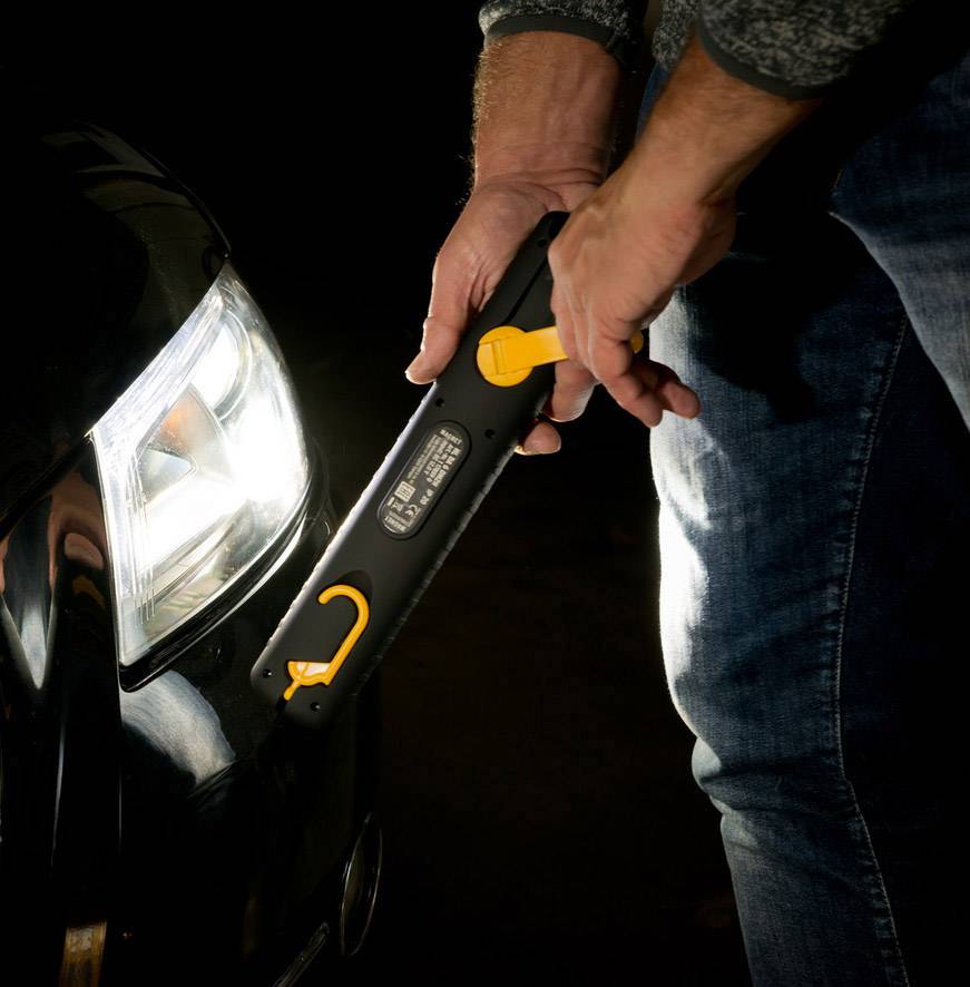 Une personne vérifie la pression d'un pneu à l'aide d'un manomètre numérique à côté d'une voiture dans l'obscurité.